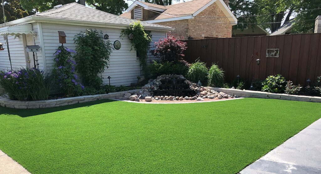 A beautiful residential yard with a water feature. The yard has lush artificial turf that appears well manicured and clean in design.